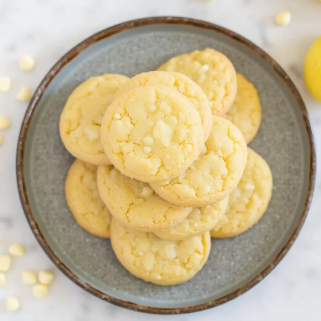 Freshly baked lemon white chocolate cookies on a tray with lemon zest and white chocolate chunks
